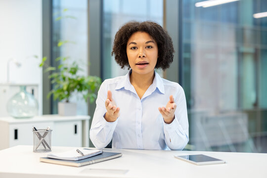 An African American businesswoman in the office is holding an online meeting on camera, gesturing with her hands and explaining