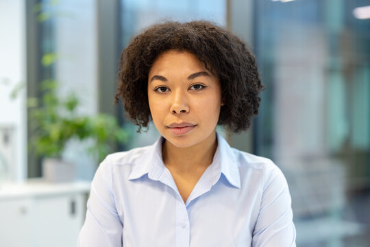 Close-up photo of a serious young African American businesswoman in a shirt sitting in the office and looking confidently at the camera