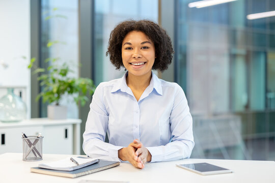 Close-up portrait of a smiling African American woman sitting at an office desk and looking at the camera