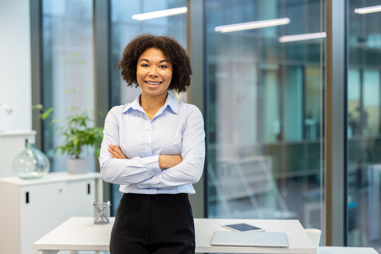 Portrait of a young African American businesswoman standing in the office, crossing her arms over her chest and looking at the camera with a smile