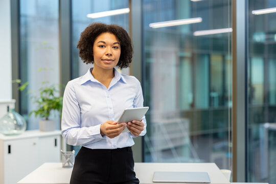 Portrait of a successful young African American businesswoman standing in the office, holding a tablet and looking confidently at the camera