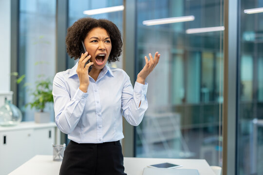 Angry young African American woman standing in office, shouting and talking on phone
