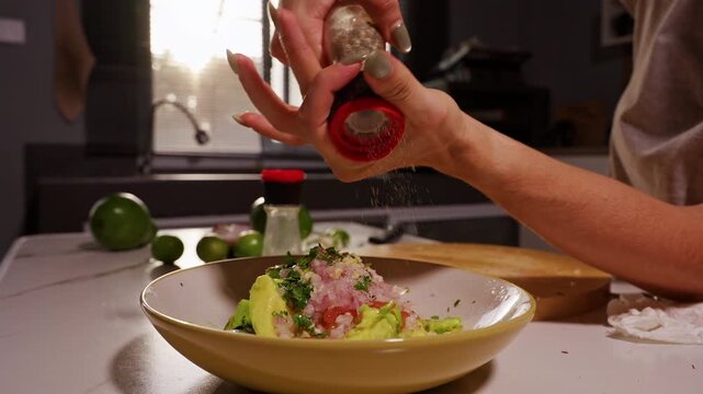 Female Hands Grind Black Pepper over Bowl of Fresh Avocado, Tomato, Onion and Cilantro, Seasoning Homemade Guacamole