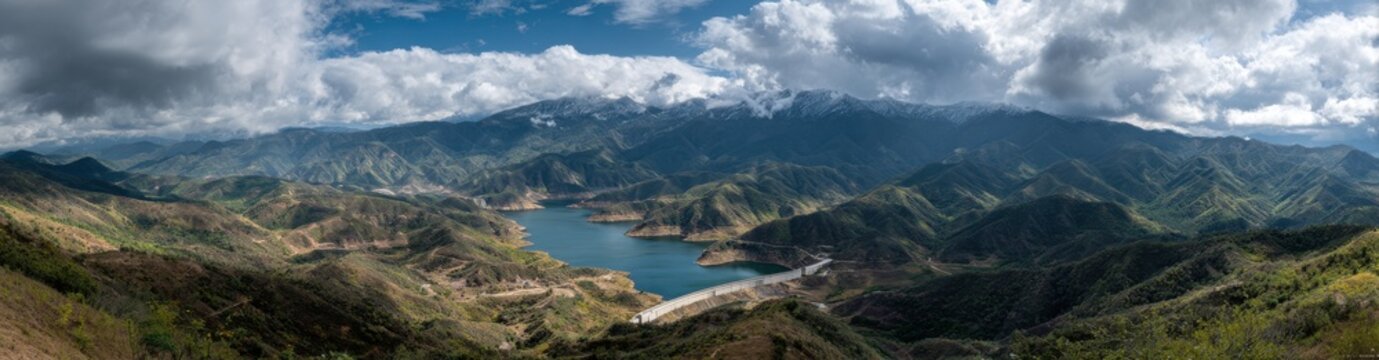 Panoramic high angle view of a blue mountain lake nestled in a valley with lush green slopes and dramatic cloudy sky in the background mountain landscape panoramic outdoors environment