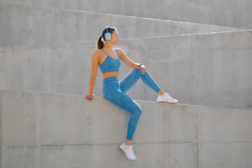 Fototapeta premium Sporty woman enjoys outdoor workout while sitting on a concrete structure in fitness gear