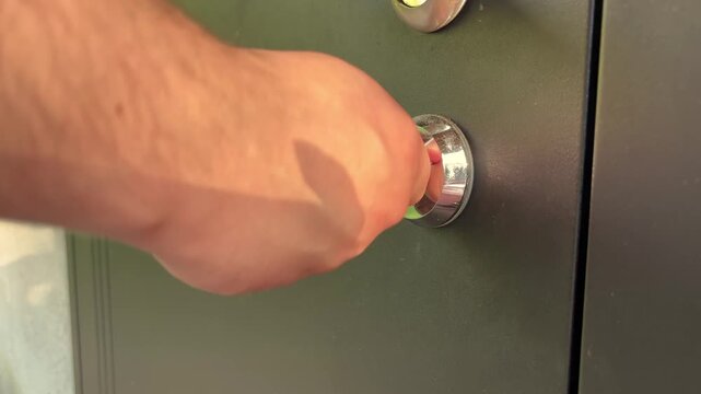 A man turns a key to lock a scratched door lock, home security, property protection, everyday safety, residential access control.