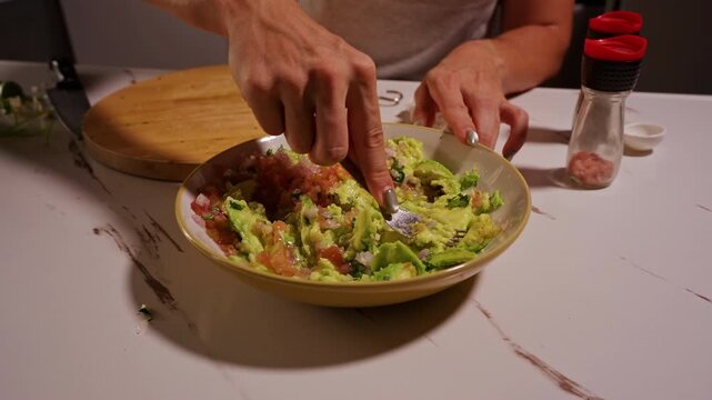 Close View of Woman Mixing and Mashing Fresh Avocado, Tomato, Onion and Cilantro with Fork, Homemade Guacamole Preparation