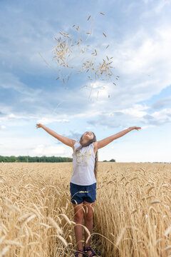 Happy little girl throwing wheat spikelets in air in golden field under blue sky