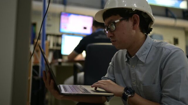 Focused professional male industrial engineer programs an advanced smart factory electrical control cabinet using automation software on a digital laptop inside a modern manufacturing plant.