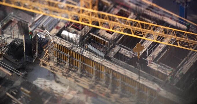 Construction site from above in Dubai, workers in green uniforms and helmets move around the formwork and rebar, yellow tower crane swings over the concrete floor, tilt shift look, timelapse