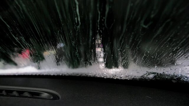 Point of view from inside an automobile going through an automatic car wash, with spinning brushes and soapy water cleaning the windshield, showcasing modern vehicle maintenance and detailing
