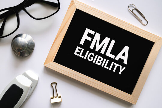 FMLA Eligibility text on black chalkboard with glasses and office supplies on white background, labor law and HR concept