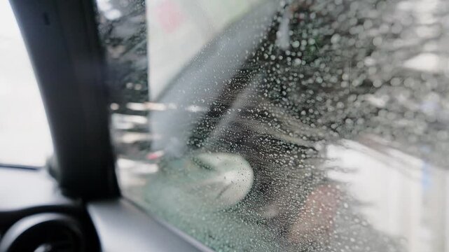 Soapy water splashing on a car window during an automatic car wash, with large rotating brushes cleaning the vehicle's exterior for a complete and thorough maintenance service