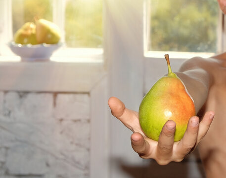 A young boy holds a ripe, colorful pear towards the camera, offering it with a smile.