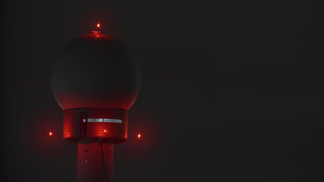 Spherical radar dome sits on top of a tower, red warning lights glow through thick night fog, radar station equipment used for weather and air navigation monitoring
