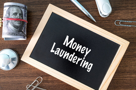 Money Laundering text on black chalkboard with dollar bills and office supplies on wooden desk, financial crime concept