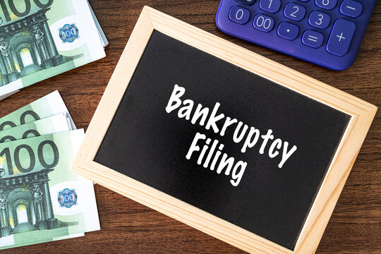 Bankruptcy Filing text on black chalkboard with euro banknotes and calculator on wooden desk, financial law concept