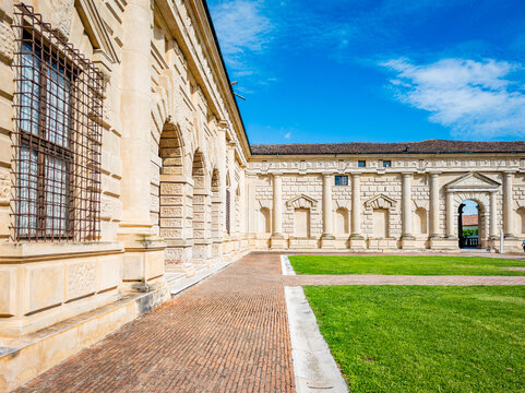 Palazzo Te showing its classical Renaissance architecture with stone walls, arches, textured pilasters, and a gridded window overlooking the spacious courtyard with green grass and brick paving