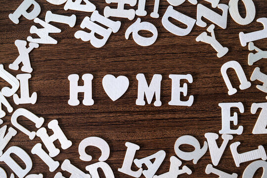 HOME word with heart symbol spelled with letter tiles on scattered letters wooden background, real estate and family concept