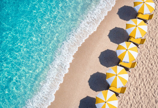 Aerial view of yellow and white beach umbrellas and lounge chairs on sandy shore