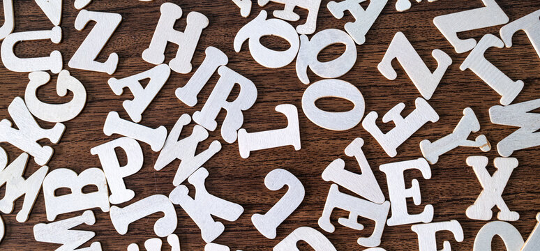 Scattered white wooden letter tiles on dark brown wooden background, education and typography abstract concept