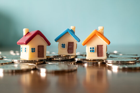 Three colorful miniature toy houses on pile of coins on blue background, real estate investment and mortgage concept