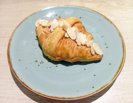 Golden Almond Croissant Served on a Blue Ceramic Plate with Wooden Table Background