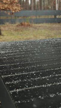 Vertical video. First snowflakes fall onto a dark wooden terrace, marking the start of winter.