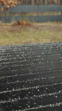 Vertical video. Gentle snowfall lands on a wooden house terrace with blurred forest in the background.