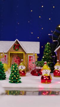 An unusual Santa Claus appears in front of the houses and snowmen with Christmas trees