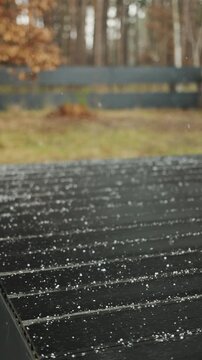 Vertical video. Fresh snowflakes cover a wooden deck outside a modern home during early winter.