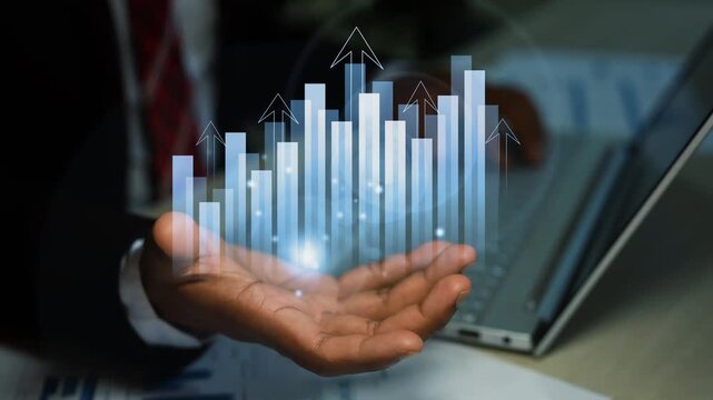 Businessman holding a glowing hologram rising bar chart over his hand beside a laptop, Business growth success finance data analysis and digital progress
