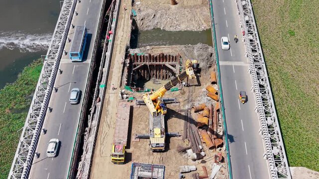 Vehicles crossing an elevated bridge beside piers under construction over a coastal waterway