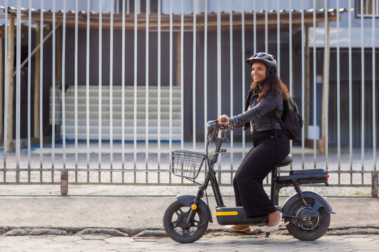 Young Black Brazilian woman commuting on an electric bicycle with helmet and backpack, representing modern urban mobility, daily transportation, and sustainable mobility.