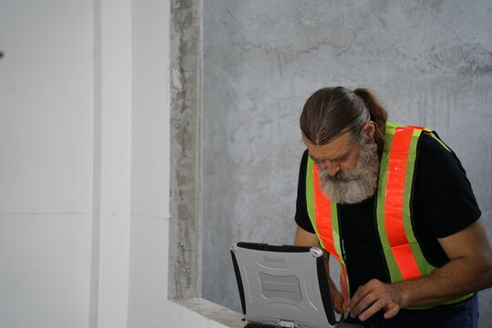 Construction Site Supervisor Using Rugged Laptop for Building Inspection and Project Management
