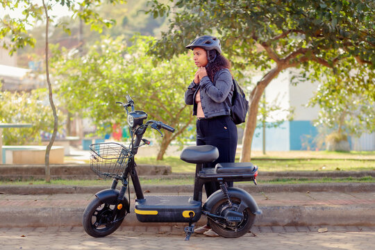 Young Black woman fastening her helmet before riding her electric bicycle to work, representing safe and sustainable daily commuting.