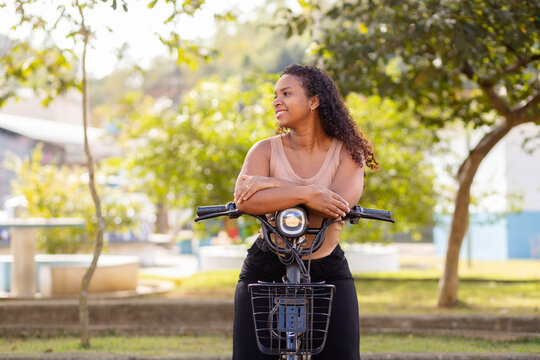 Young Black Brazilian woman enjoying a break with her electric bicycle, representing urban mobility, everyday commuting, and sustainable transportation.