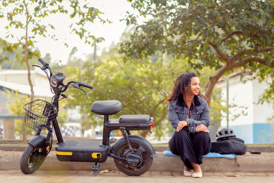 Young Black Brazilian woman relaxing beside her electric bicycle, representing urban mobility, everyday transportation, and sustainable mobility.