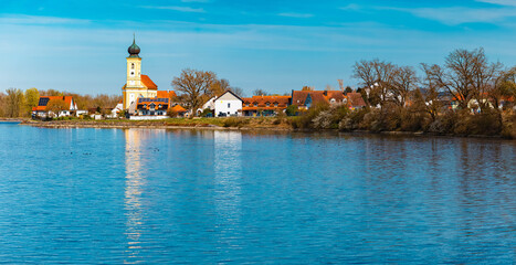Fototapeta premium Spring landscape on a sunny day with reflections and a church at Echinger Stausee reservoir, Eching, Landshut, Bavaria, Germany