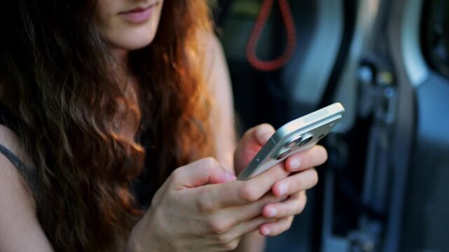 Close-up of a woman using a smartphone to send text messages while sitting in a parked SUV, illustrating mobile communication, digital messaging, online chatting, and modern technology.