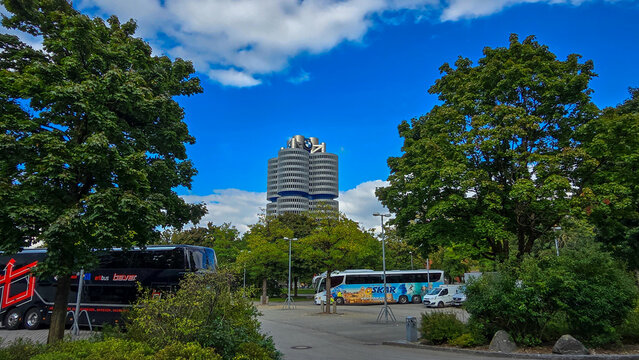 Munich, Germany - September 27, 2025. Scenic view of iconic BMW four-cylinder skyscraper under blue sky with tourist buses.