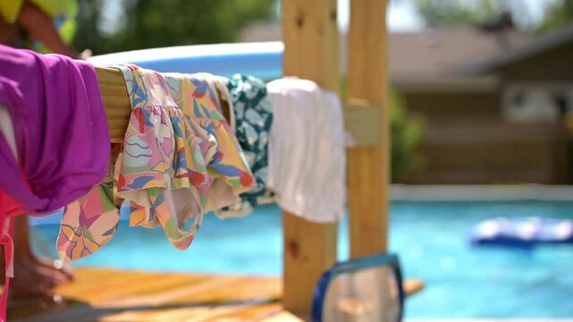 Colorful bathing suits hanging to dry beside a sparkling backyard swimming pool on a sunny summer day
