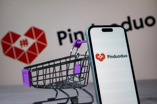 Pinduoduo chinese e-commerce platform logo on smartphone screen next to miniature shopping cart.