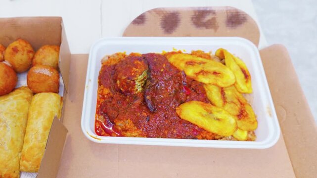 West African takeout boxes with jollof rice plantain and pastries