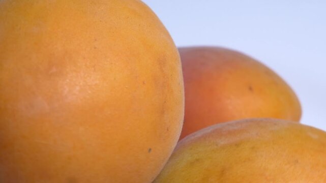 Close-up of fresh orange apricots rotating on a white plate, showcasing their soft fuzzy skin and vibrant summer color under studio lighting.