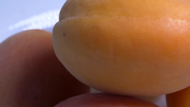 Close-up of fresh orange apricots rotating on a white plate, showcasing their soft fuzzy skin and vibrant summer color under studio lighting.