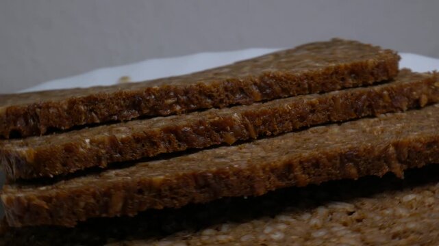 Close-up of dark whole grain rye bread slices rotating on a white plate, showcasing their rich grain texture and healthy crust under studio lights.
