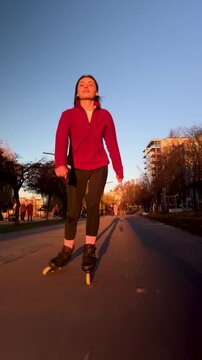 Woman on inline skates rides through city walkway at golden hour. Vertical footage emphasizes movement, balance, and healthy lifestyle in warm natural light