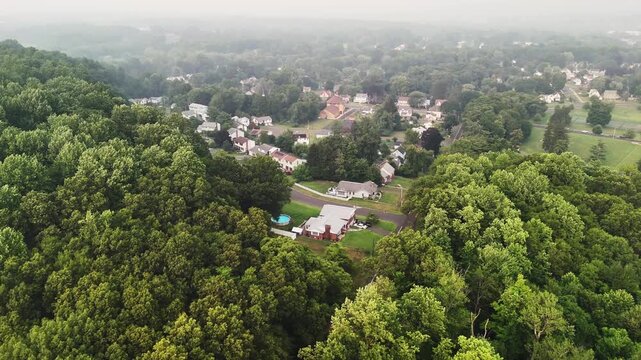 Aerial footage of thick wildfire haze above a green forest and suburban neighborhood in the USA, highlighting natural disaster, smoke pollution, and climate risk.
