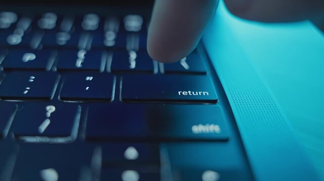Finger clicking on Return or Enter key on laptop keyboard at night in dark room. Working late in office or home studio. Programmer or hacker starts or initiates task action on application software